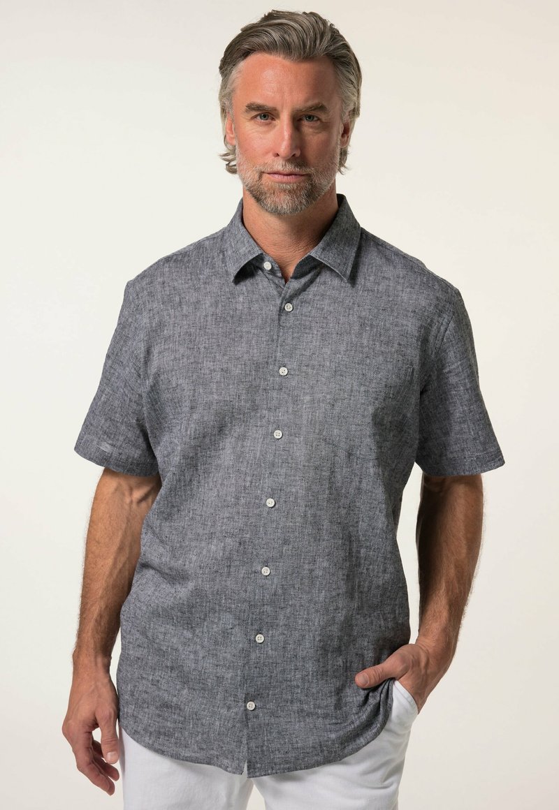 Camicia a maniche corte con bottoni in tessuto grigio scuro e texture, con colletto, tasca frontale e bottoni bianchi. Indossata con pantaloni bianchi.