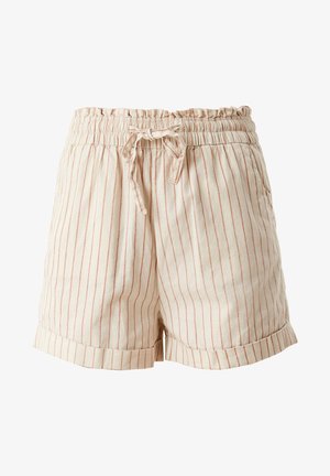 Donna che indossa un top a maglia color ruggine, pantaloncini crema a vita alta con righe verticali e sandali beige chunky, in piedi all'interno di un ambiente.