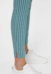 Turquoise geprinte enkelbroek van een zachte stof, met een zigzagpatroon en een gespleten zoom, gecombineerd met witte sneakers.
