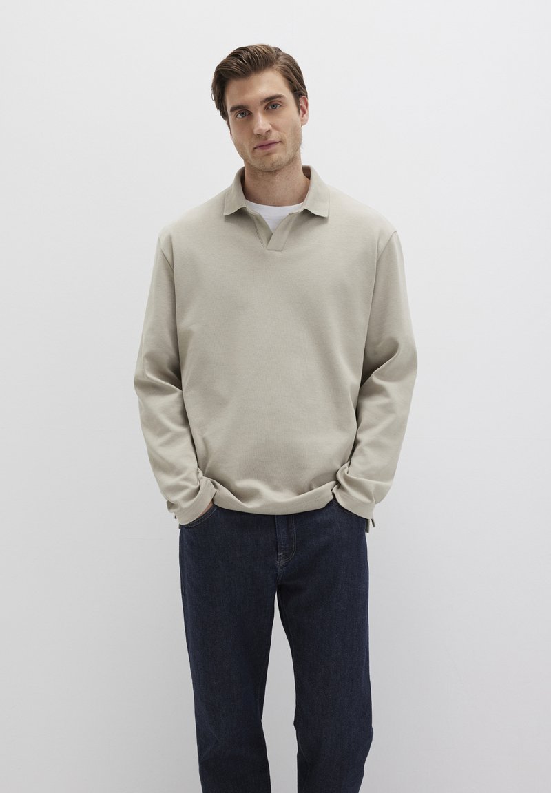 Beige pullover with a v-neck and long sleeves, made from soft material. Paired with dark denim jeans, featuring a relaxed fit.