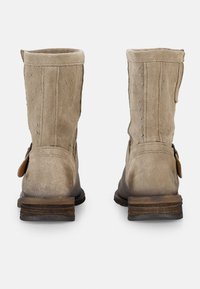 Botas de tobillo de ante beige con lados texturizados, suela marrón en contraste y pequeña correa decorativa en el lado exterior.