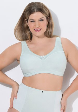 Smilende kvinde med skulderlangt hår iført lyseblå støttende bh og matchende høj talje trusse mod enkel hvid baggrund.