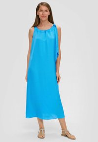 Blaues ärmelloses Kleid aus strukturiertem Stoff, mit rundem Ausschnitt und seitlichem Bindeband, das bis zur Mitte der Waden reicht. Kombiniert mit flachen Sandalen.