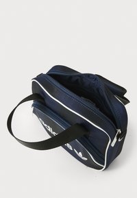 Navy blue zippered pouch made of durable fabric. Features a white accent stripe and an exterior pocket with branding. Black handle for carrying.