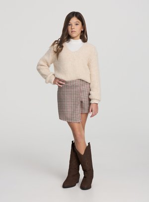 Maglione in maglia crema con scollo a v, minigonna a quadri in toni marroni e rossi, e stivali da cowboy in suede marrone con ricami intricati.