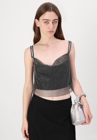 Svart mesh crop topp med prikkemønster, med brede stropper og logo. Kombinert med en svart skjørt og en sølv sateng håndveske.