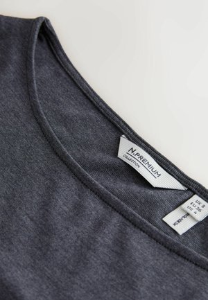 Tumši pelēka t-krekls ar apaļu kakla izgriezumu un gludu faktūru. Etiķete iekšpusē rāda zīmola nosaukumu un izmēra informāciju.