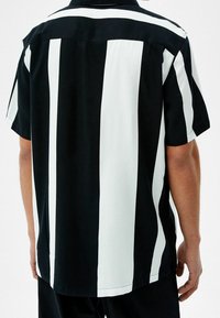 Lyhythihainen paita, jossa on pystysuorat mustavalkoiset raidat, räätälöity kaulus ja rento istuvuus suoralinjaisella helmalla.