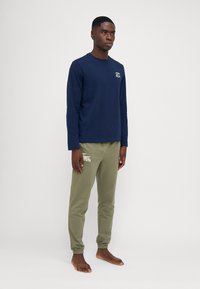 T-shirt à manches longues bleu marine avec un petit logo, associé à un jogging vert olive ornée d'un logo de marque blanc. Matière en mélange de coton doux.