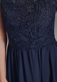 Marineblaues Kleid mit einem bestickten Blumen-Spitze-Oberteil mit Perlen, fließendem Rock und einem weichen, strukturierten Stoff.