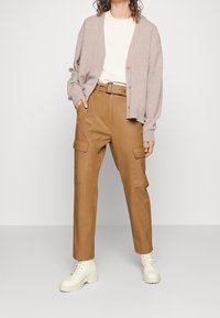Hellbrauner, kabelstrick gestrickter Cardigan, beiges T-Shirt, sandfarbene Cargo-Hosen mit Taschen und cremefarbene Schnürstiefel. Weicher Stoff und lockere Passform.