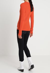 Ribbat, långärmad, orange stickad topp som matchas med svarta skinnyjeans och vita ankelstövlar med klack och enkel design.