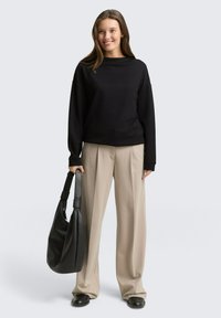 Schwarzer, gerippter Sweatshirt mit Bootsausschnitt, kombiniert mit beigen, weit geschnittenen Hosen. Trägt eine strukturierte schwarze Hobo-Tasche. Glatte Lederschuhe.