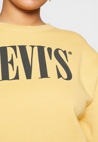 Sudadera amarilla hecha de una tela suave, con el gran texto negro "LEVI'S" en el pecho. Diseño clásico de cuello redondo, textura lisa.