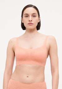 Bralette de cor pêssego com um padrão texturizado, alças largas e uma bainha em forma de escalope. Feito de um tecido macio e elástico para maior conforto.