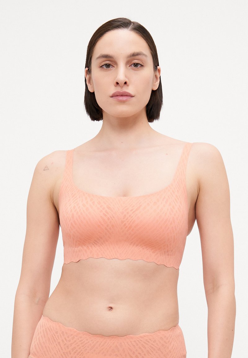 Bralette de cor pêssego com um padrão texturizado, alças largas e uma bainha em forma de escalope. Feito de um tecido macio e elástico para maior conforto.