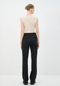 Top sin mangas ajustado color beige combinado con pantalones negros de tiro alto que cuentan con dos bolsillos traseros, tejido suave y diseño de pierna recta.