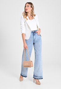 Blazer blanc ajusté sur un top blanc, associé à un jean large taille haute bleu clair. Comprend un sac beige avec une chaîne et des talons nus.
