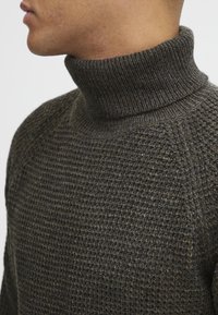 Dunkelgrauer, gestrickter Rollkragenpullover mit strukturiertem Waffelmuster, geripptem Kragen und tailliertem Schnitt. Weiches Material mit subtiler Satinoberfläche.