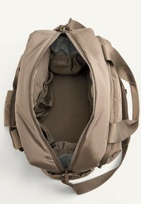Borsa da viaggio morbida beige in tessuto, con ampia tracolla, apertura superiore con zip e numerose tasche elastiche spaziose all'interno.