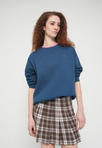 Μπλε φούτερ με ροζ γιακά, άνετη εφαρμογή, πυκνό υλικό. Συνδυασμένο με καφέ και λευκή καρό πλισέ φούστα, υφασμάτινη υφή.