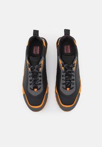 Le sneaker nere e arancioni presentano una tomaia in pelle liscia, dettagli testurizzati, colletto imbottito e lacci neri con un design di suola robusto.