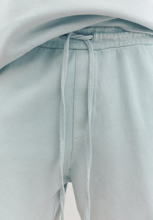 Közeli kép világoskék melegítőnadrágról, melynek derékrészén egyszerű csomóval megkötött zsinór található.