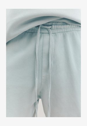 Nahaufnahme von hellblauen Jogginghosen mit einer im Bund zu einem einfachen Knoten gebundenen Kordel.