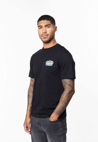 Svart t-shirt i bomull med en liten, färgglad grafik på vänster bröstområde. Kortärmad och med klassisk passform.