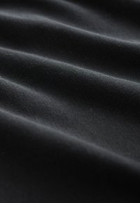 Musta kangas, jossa on sileä pinta, pehmeitä poimuja ja hentoa kiiltoa. Pinta näyttää kudotun kuvion, joka korostaa värin syvyyttä.