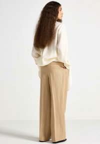 Krämfärgad linne skjorta med långa ärmar, ihopparad med beige vida byxor som har en strukturerad yta och två bakfickor.