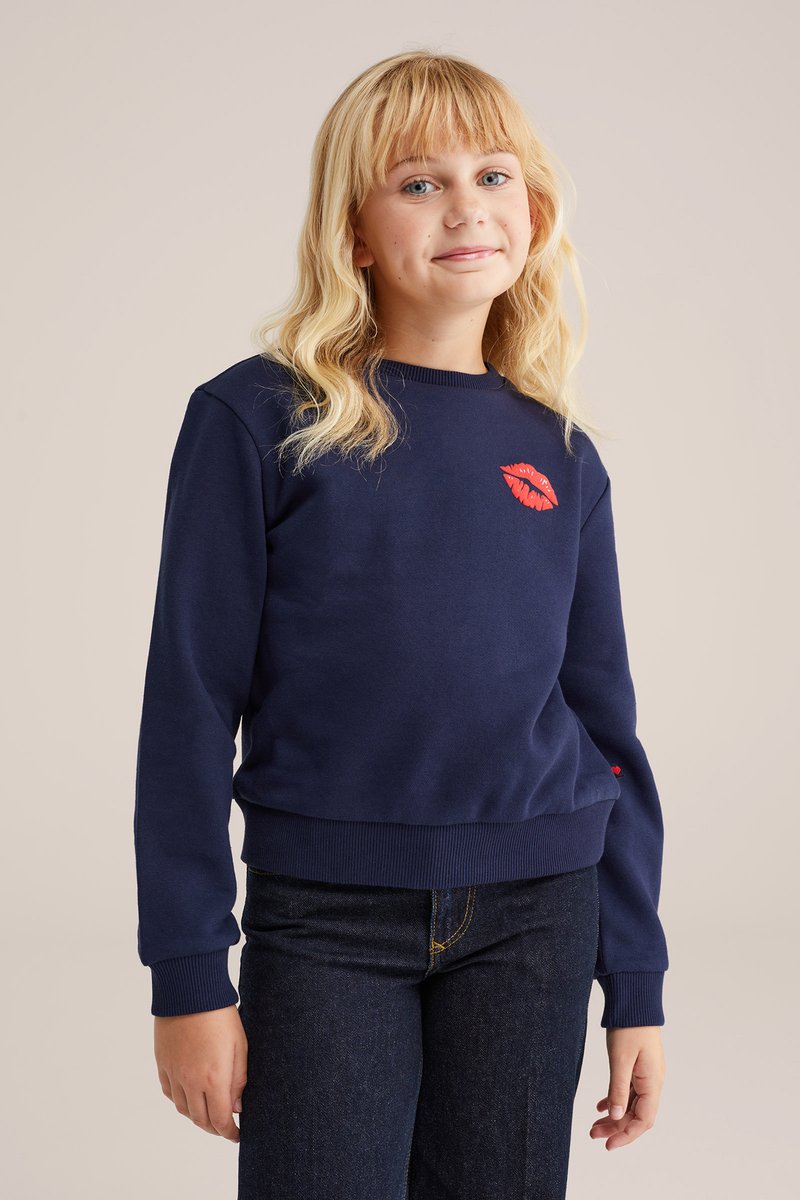 Mornarska majica s dugimi rokavi, rebrastimi manžetami in robom. Na prsih je grafika rdeče ustnice. Mehka, teksturirana tkanina.