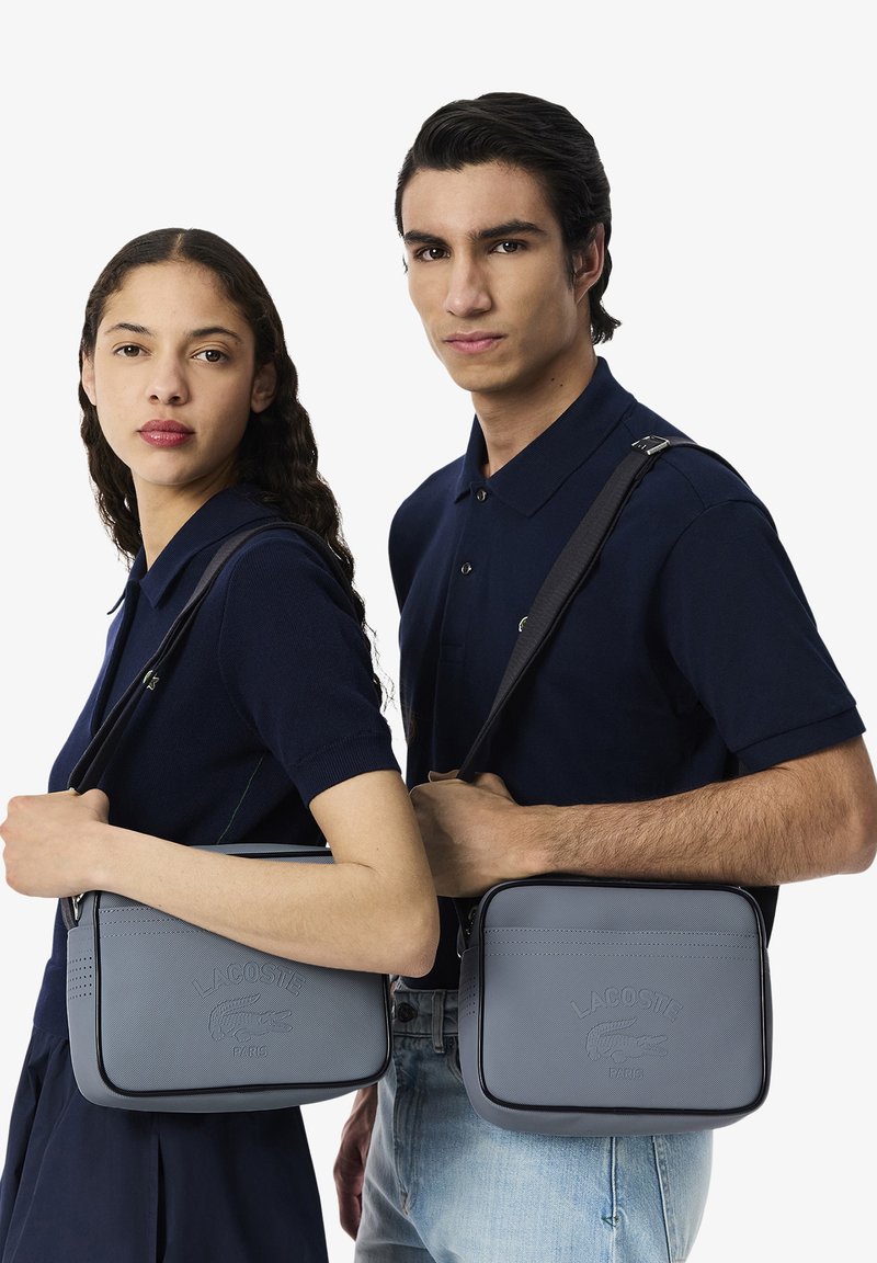 Borse a spalla Lacoste grigie, realizzate in materiale testurizzato, con logo in rilievo, dettagli laterali e tracolle regolabili.