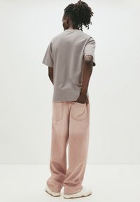 Grå bomulds T-shirt med korte ærmer, kombineret med løse, lyserøde denimjeans. Hvide sko fuldender outfittet.