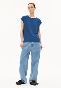 Haut bleu à manches courtes avec un col rond, associé à un jeans taille haute bleu clair à jambes larges et des chaussures à enfiler noires avec des franges. Texture en coton lisse.