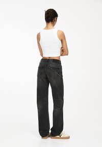 Jeans in denim nero con una vestibilità ampia, abbinati a un top corto bianco, che mostrano una texture liscia e un design minimalista.
