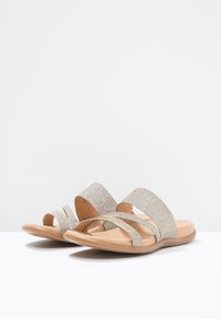 Sandales à brides avec deux larges bandes métalliques dorées et une semelle intérieure marron. Les brides ont une finition texturée et scintillante. Semelle plate.