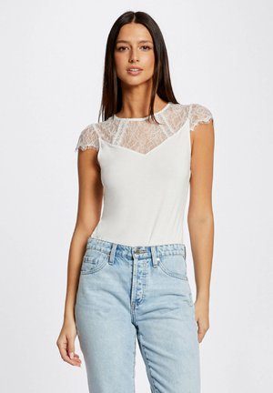 T-shirt blanc avec des inserts en dentelle aux épaules, muni d'un col en scoop et de manches courtes, associé à un jean taille haute bleu clair.