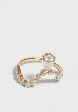 Bague en or avec un diamant en forme de poire et une rangée courbe de diamants ronds sur fond blanc.
