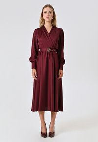 Abito avvolgente bordeaux realizzato in tessuto morbido, con maniche lunghe, vita stretta con una cintura decorativa e gonna midi.