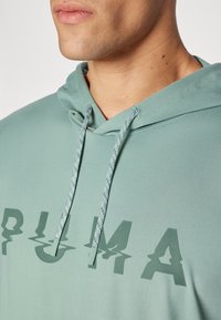 Felpa verde chiaro con cappuccio regolabile, caratterizzata da un grande logo testurizzato sul petto. Tessuto morbido e vestibilità rilassata.