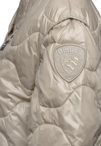 Beige, gewatteerde pufferjack met een gestructureerde afwerking. Heeft een geborduurd Blauer-logo op de schouder.
