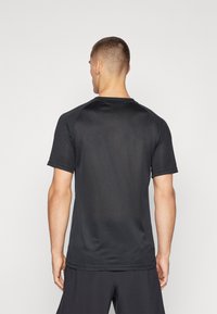 Camiseta atlética negra, de manga corta, hecha de un material ligero y texturizado, con un cuello redondo y sutiles detalles de costura.