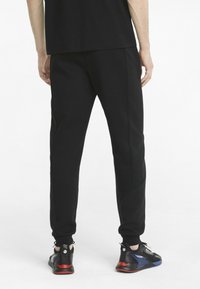 Sorte atletikbukser med en struktureret sidepanel, elastisk talje og tætsiddende manchetter, kombineret med sorte og røde sneakers.