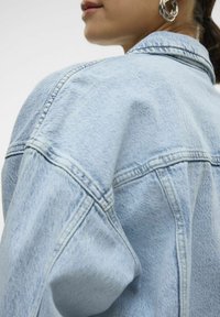 Svetlo modra jeans jakna z oversize krojem, vidno šivanje in klasičen ovratnik. Ima teksturirano blago in ukrivljene ramenske šive.