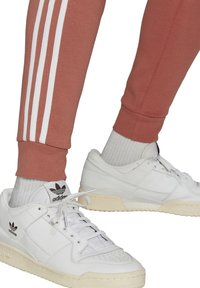 White leather sneakers with a textured upper and perforated details, paired with fitted pink sweatpants featuring three white stripes.