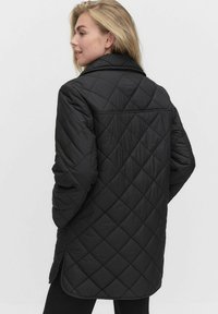 Svart kviltad jacka med hög krage, som har ett strukturerat diamantmönster, långa ärmar och en lätt svängd fåll.