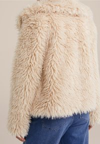 Faux fur-jacka i ljusbeige med en strukturerad, shaggy yta. Den har en bred krage och ett kortat fåll, kombinerad med blå denim.