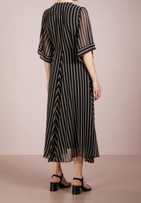 Musta-valkoinen raidallinen midi-mekko, jossa on läpinäkyvät hihat, tiukka yläosa ja volyymikas hame. Mekossa on kerrostettu tekstuuri ja vaatimaton pääntie.