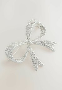 Broșă argintie în formă de arc, împodobită cu pietre strălucitoare clare, având un finisaj metalic neted și un design structurat cu capete ascuțite.